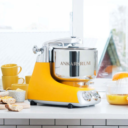 Ankarsrum stand mixer in sunrise yellow, shown on a countertop.